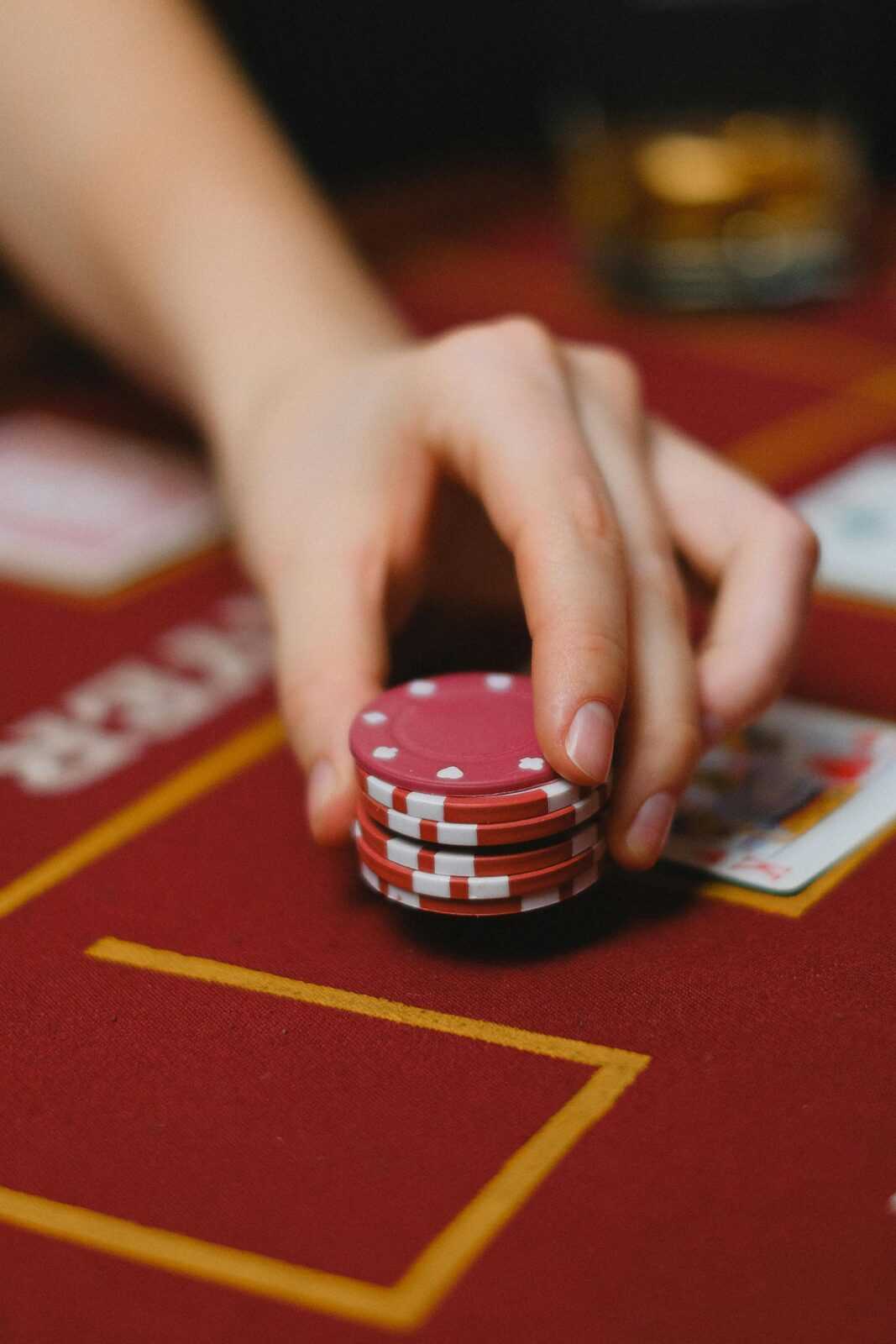 A detailed close-up of a hand holding red poker chips on a casino table.